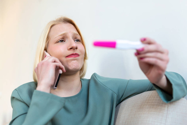 妊娠検査の対照ラインを見てショックを受けた女性.独身の悲しい女性は妊娠検査を開催不平を言う。陰性の妊娠検査をしている抑うつ女性. - 写真・画像