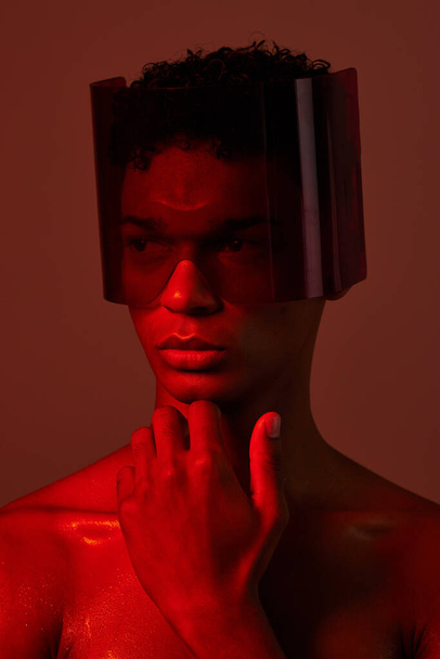 man, face and red light with futuristic glasses for edgy cyberpunk fashion, modern gen z fantasy and sci fi model for beauty. Young black man, vision thinking or designer neon lighting studio. - Photo, Image