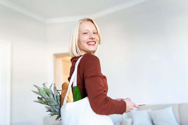 Mulher bonita com legumes em bolsa de supermercado em casa. Retrato de uma jovem feliz segurando um saco cheio de vegetais saudáveis em casa. Alimentos saudáveis primeiro
 - Foto, Imagem
