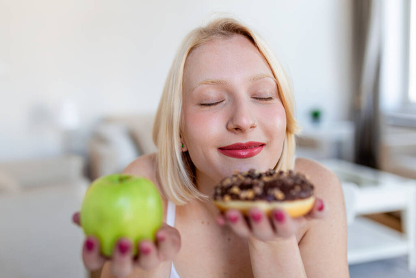 Який вибрати здоровий чи здоровий. Портрет красивої молодої жінки, яка вибирає між яблуком або пончиком
 - Фото, зображення