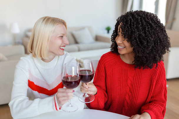 Дві подружки проводять час разом вдома, сидячи на дивані. копіювання простору. Веселі жінки п'ють вино
 - Фото, зображення