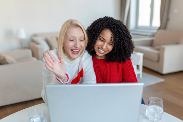 Deux belles femmes utilisant un ordinateur portable pour un appel vidéo en ligne et un toast en ligne avec leurs amis. Partie en ligne pour les amis. - Photo, image