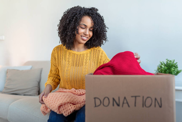 Donation Concept. Woman holding a Donate Box with full of Clothes. Woman holding a book and clothes donate box. Clothes in box for concept donation and reuse recycle - Zdjęcie, obraz