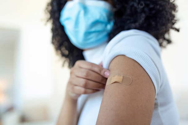 アフリカ人女性は予防接種を受けた後、シャツの袖を持ち、包帯で腕を見せていた。covid 19の予防接種 - 写真・画像