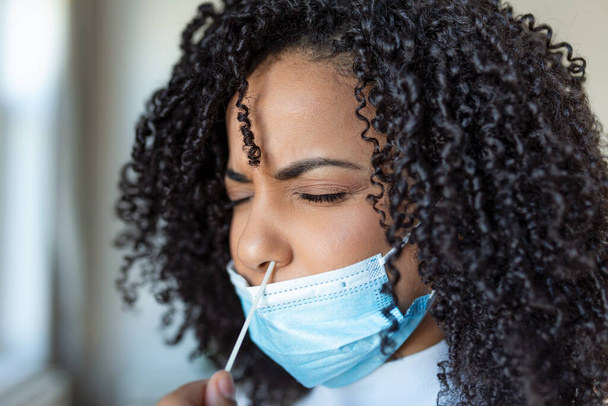 Mujer afroamericana joven que se toma una prueba casera de autolavado para COVID-19 en casa con un kit de antígeno. Introducir la varilla nasal para comprobar la infección del Coronavirus. Cuarentena, pandemia. - Foto, Imagen