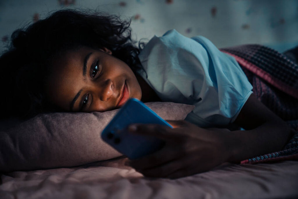 African teen girl using phone before sleep in dark room at home - Fotoğraf, Görsel