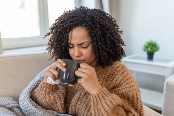 Sick young woman sitting at home in bed with hot cup of tea and handkerchief. Seasonal colds, cough, runny nose, viral infections, home treatment - Photo, image
