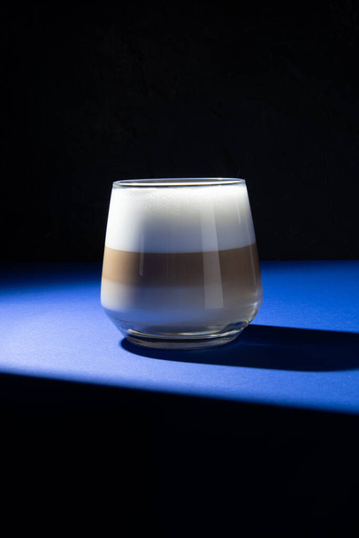 Latte-Kaffee in einem transparenten Glas auf dunkelblauem Hintergrund. Beleuchtung im Studio. - Foto, Bild