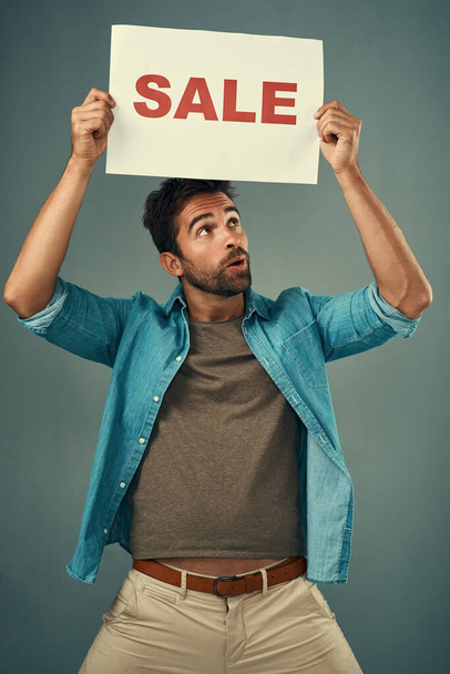 Who doesnt get excited when they see a sale sign. Studio shot of a handsome young man holding a sale sign against a grey background - Fotoğraf, Görsel