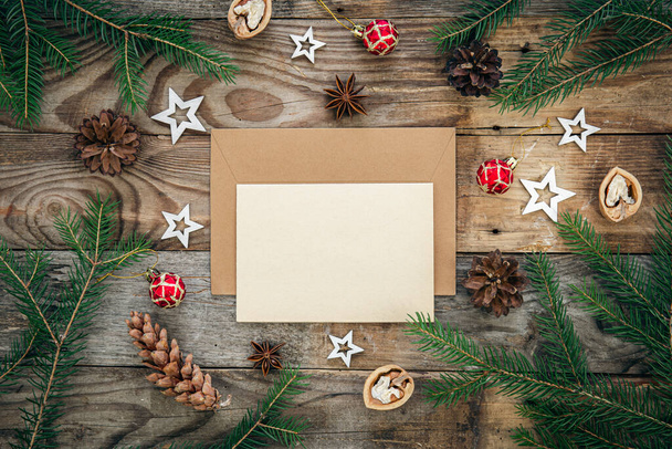 Пустая бумага, конверт на деревянном фоне с ветками елки и рождественским декором, плоский уголок. - Фото, изображение