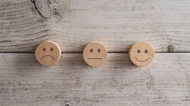 Three wooden cut circles each with a different emoticon - sad, average and smiling. Conceptual image of customer satisfaction and rating. Over white wooden background. - Photo, Image