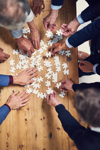 Teamwork wird alle Lösungen bieten. Aufnahme einer Gruppe von Geschäftsleuten, die in einem Büro gemeinsam ein Puzzle zusammenbauen - Foto, Bild