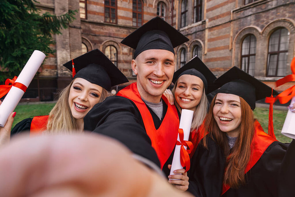 groupe heureux diplômés étudiants utilisent le téléphone mobile pour prendre selfie ensemble. Après avoir reçu des diplômes. - Photo, image