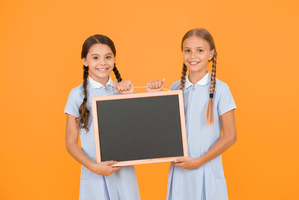 cheerful friends in retro uniform. vintage kid fashion. back to school. small girls hold blackboard. children education. girls presenting information. old school. copy space on board. advertising. - Photo, image