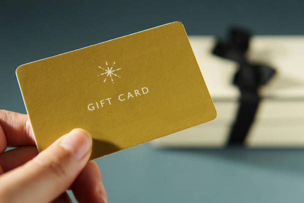 Hand holding a yellow gift card against a gift box background - Φωτογραφία, εικόνα