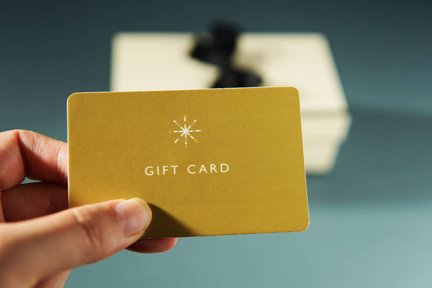 Mano sosteniendo una tarjeta de regalo amarilla contra un fondo de caja de regalo - Foto, imagen