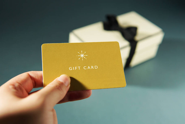 Χέρι κρατώντας μια κίτρινη κάρτα δώρο σε φόντο κουτί δώρου - Φωτογραφία, εικόνα