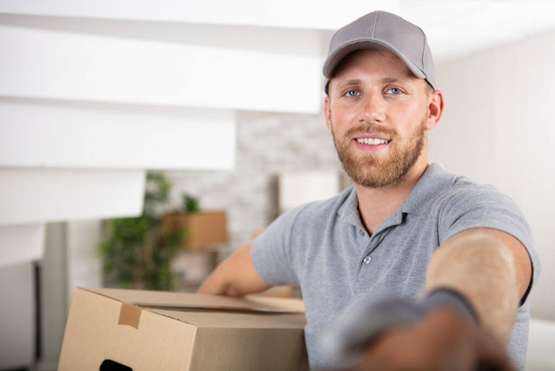 smiling young delivery man holding a cardboard box - Фото, зображення