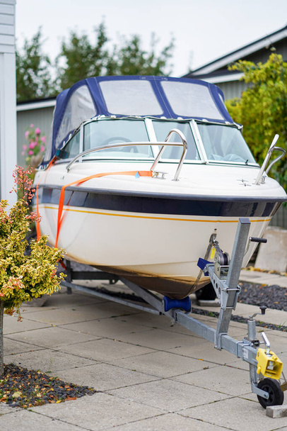 Piccola barca a motore su rimorchio parcheggiata nel vialetto vicino alla casa. Foto di alta qualità - Foto, immagini