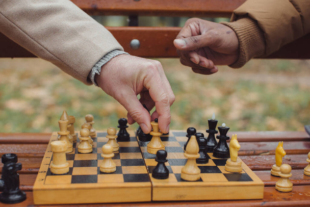 Multiethnische Männer, die im Herbst Schach spielen, parken auf einer Bank. Nahaufnahme. - Foto, Bild