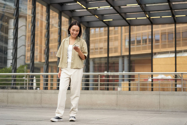 Портрет азиатской модели с телефоном. Молодая корейская девушка держит смартфон на улице, используя телефон. - Фото, изображение