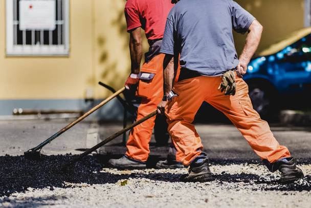 Trabajadores de la construcción durante las obras de asfalto de carreteras con monos. Trabajo manual en obra
. - Foto, imagen