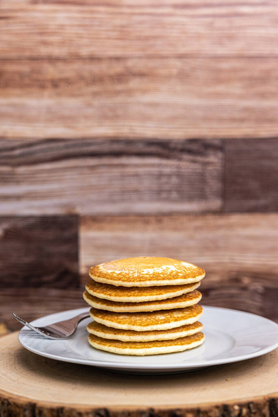 A large plate stack of pancakes with a fork against a wood background with copy space. - 写真・画像