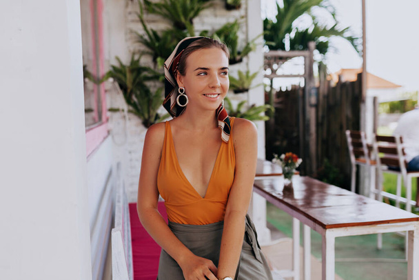 Romantic pretty girl with wonderful smile wearing summer bright clothes sitting on bright summer terrace and looking aside in summer warm day.  - Photo, Image