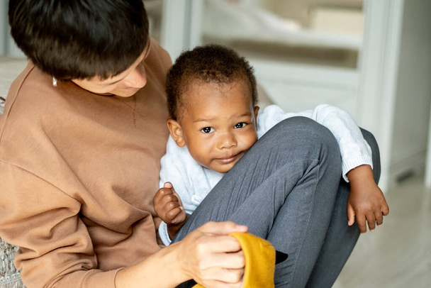 Prendersi cura della donna caucasica abbracciando il bel bambino afroamericano, la madre che gioca con il suo piccolo figlio sul pavimento, la famiglia, il programma di adozione - Foto, immagini