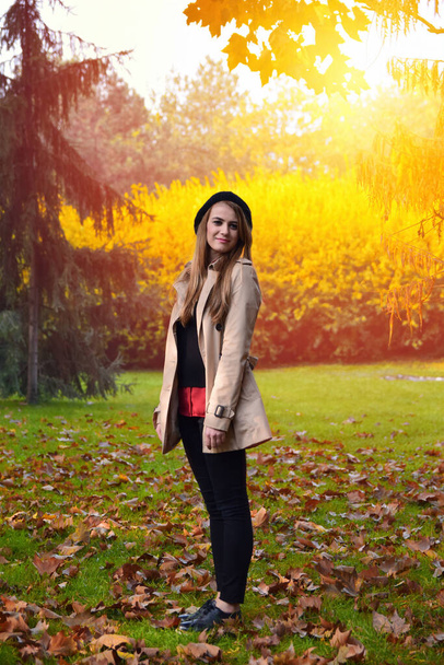 Front view of elegant young woman in cream color casual coat in autumn. Cute model stands in the park in golden autumn against background of nature.  - Photo, Image