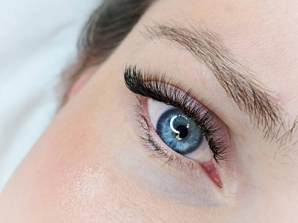 Nahaufnahme des geöffneten blauen Auges mit Wimpernverlängerungen im Schönheitssalon Makroansicht.  - Foto, Bild
