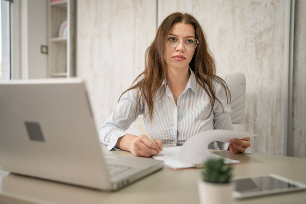 女性の一人白人起業家女性または秘書が彼女のオフィスに座ってデスクワークで紙の書類をチェック契約書の着用シャツのコピースペース - 写真・画像
