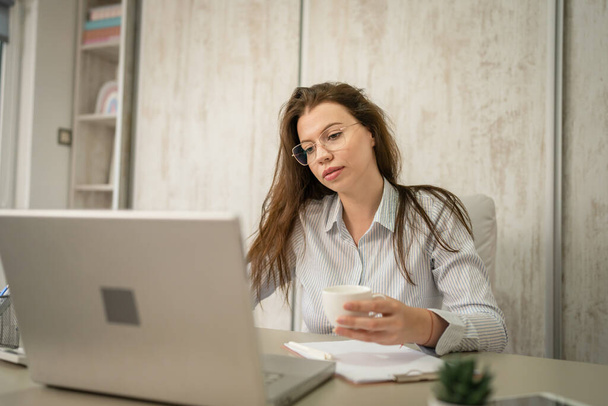 Egy nő kaukázusi vállalkozó üzletasszony vagy titkárnő ül irodájában asztali munka laptop számítógép visel inget helyet - Fotó, kép