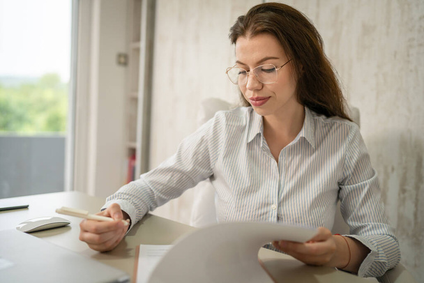 One woman female caucasian entrepreneur businesswoman or secretary sitting at her office at desk work checking paper documents contract wear shirt copy space sign contract - Foto, immagini