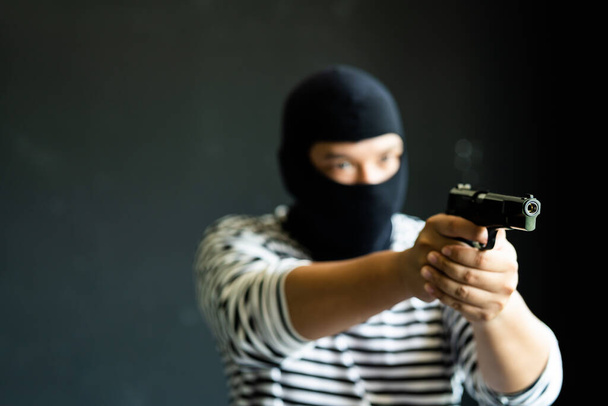 Masked robber with gun. Concept of crime and fire arm assault with mature man. Armed robbery on black.  - 写真・画像