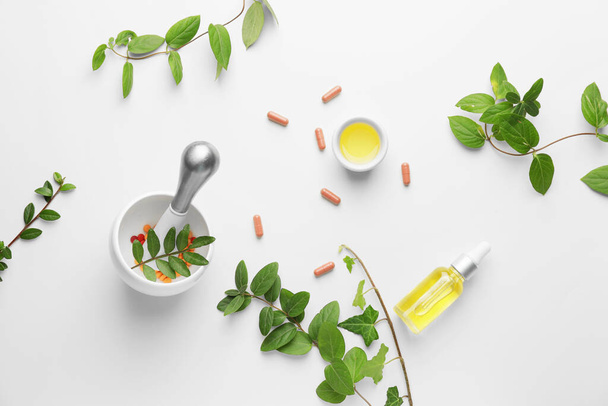 Argamassa, diferentes ervas, comprimidos e garrafa de óleo essencial sobre fundo branco - Foto, Imagem