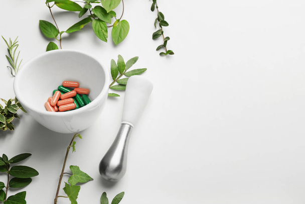 Mortar with pills, pestle and different herbs on white background - Фото, зображення