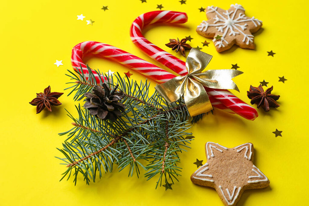 Composición navideña con rama de abeto, bastones de caramelo, galletas y especias sobre fondo amarillo - Foto, Imagen