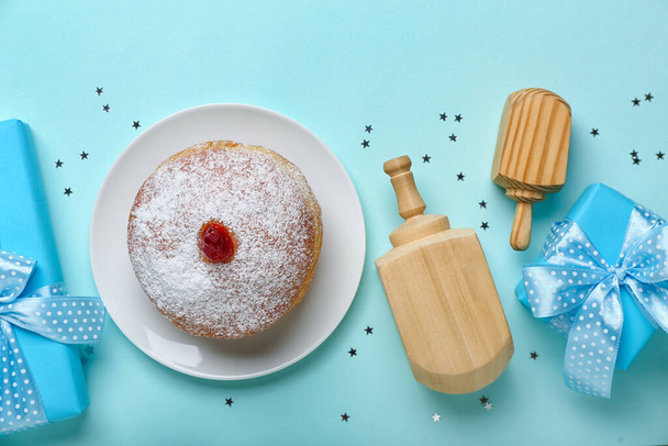 Тарелка с вкусным пончиком, дрейделями и подарками для празднования Хануки на синем фоне - Фото, изображение