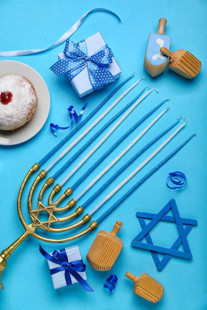 Plate with doughnut, menorah, dreidels and gifts for Hanukkah celebration on blue background - Photo, Image