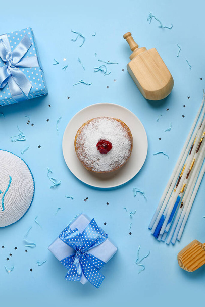 Тарелка с пончиками, свечами, дрейделями и подарками для празднования Хануки на синем фоне - Фото, изображение