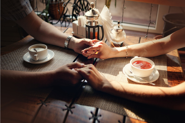 Rękach faceta i rękę dziewczyny przy stole z filiżanką herbaty i kawy - Zdjęcie, obraz