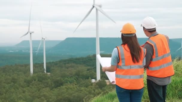 Mies- ja naisinsinöörit työskentelevät tuulipuistossa vuoren huipulla maaseudulla. Progressiivinen ihanteellinen uusiutuvan ja kestävän energian tulevalle tuotannolle. - Materiaali, video