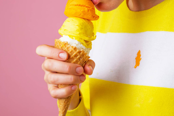 Unrecognizable woman eating ice cream cone with three scoops of different flavor. Dirty frozen dessert stain on clothes. isolated. High quality photo - Photo, Image