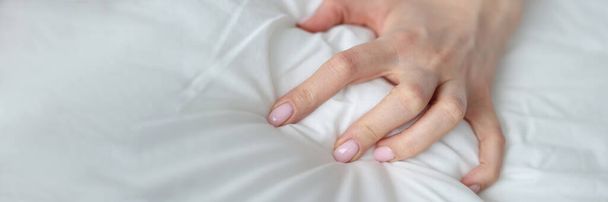 Close-up of sexy female hand pulling and squeezing white sheets in bed. Tender woman hand with sensual manicure. Sexy, pleasure and erotic concept - Foto, imagen
