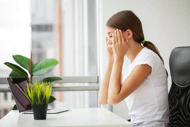 Beautiful stressed young office worker sitting at desk holding head because of pain in office. - Foto, Imagen