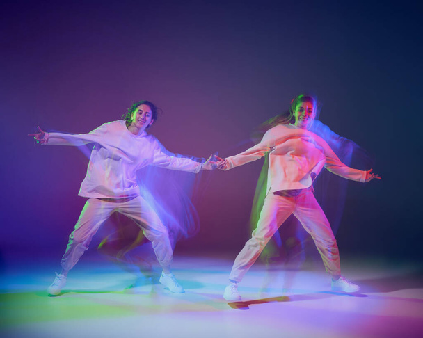 Retrato de meninas dançando hip-hop isolado sobre gradiente azul fundo roxo em néon com luz mista. Dança moderna. Conceito de movimento, cultura juvenil, estilo de vida ativo, ação, dança de rua - Foto, Imagem