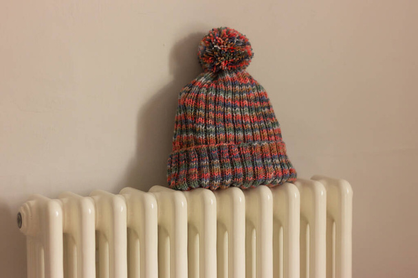 ζεστό καπέλο πλέξιμο στο ψυγείο στο δωμάτιο. θέρμανση στο σπίτι, διατήρηση θερμότητας και εξοικονόμηση ενέργειας. στεγνώματα - Φωτογραφία, εικόνα