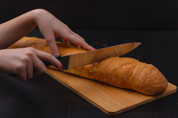 vrouwelijke handen die brood snijden op een snijplank op een houten ondergrond - Foto, afbeelding