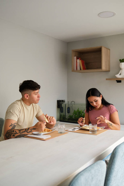 Zwei junge hispanische Leute essen traditionelle Arepas im Wohnzimmer. - Foto, Bild